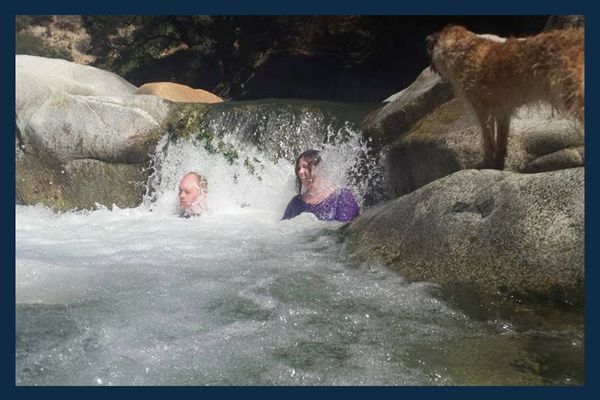 2 people in a waterfall at the Yuba River with a border terrier